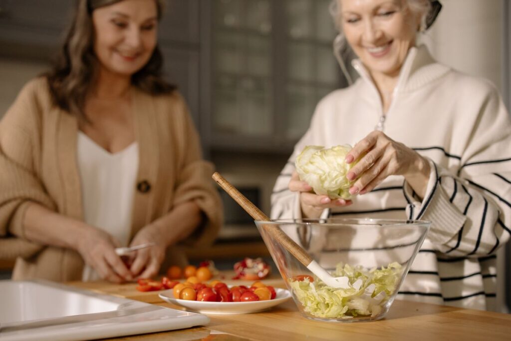 Two women smiling while preparing a fresh salad together in a kitchen