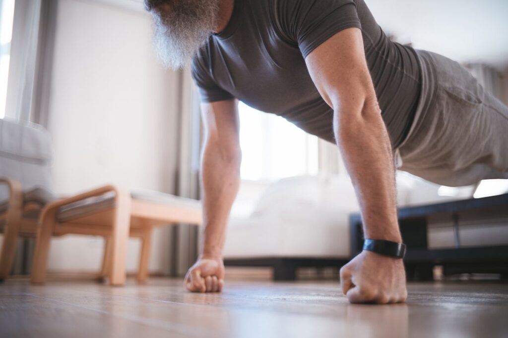 A man with a grey beard holding a plank push-up position at home